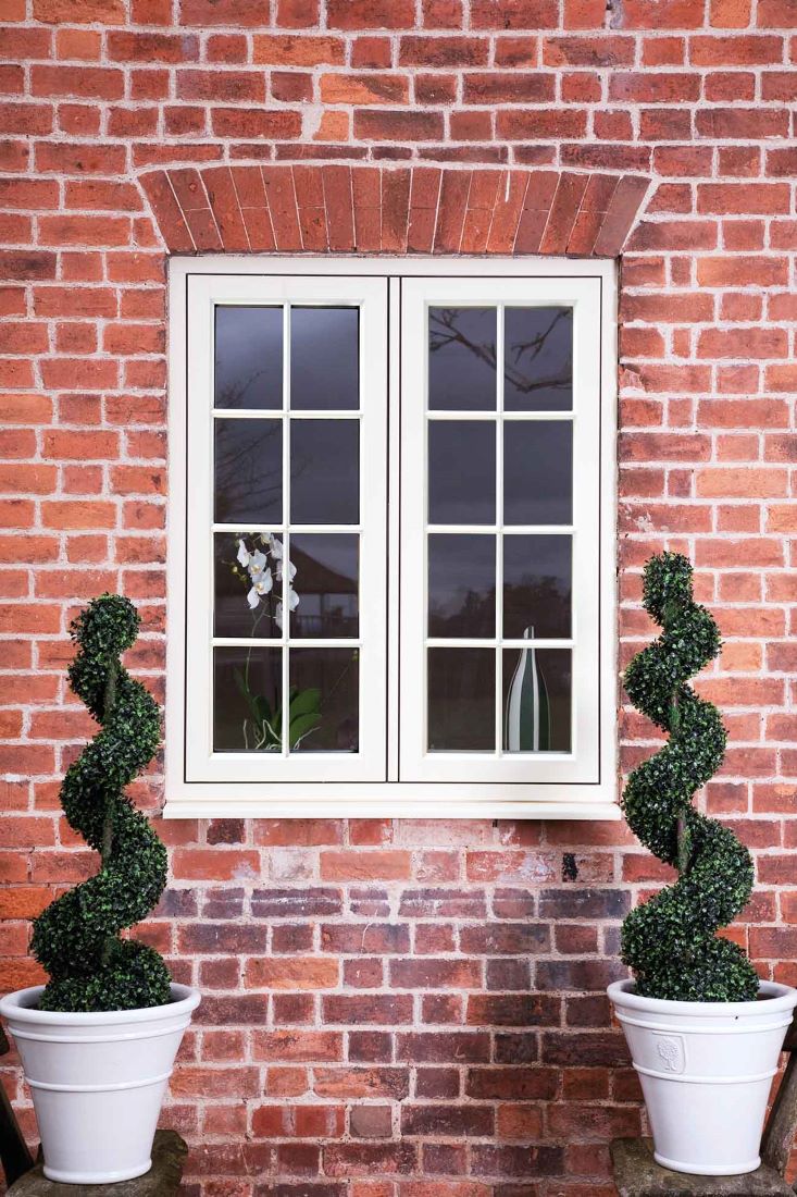 residence 9 windows in the middle of a red brick wall flanked by two tall woven plants